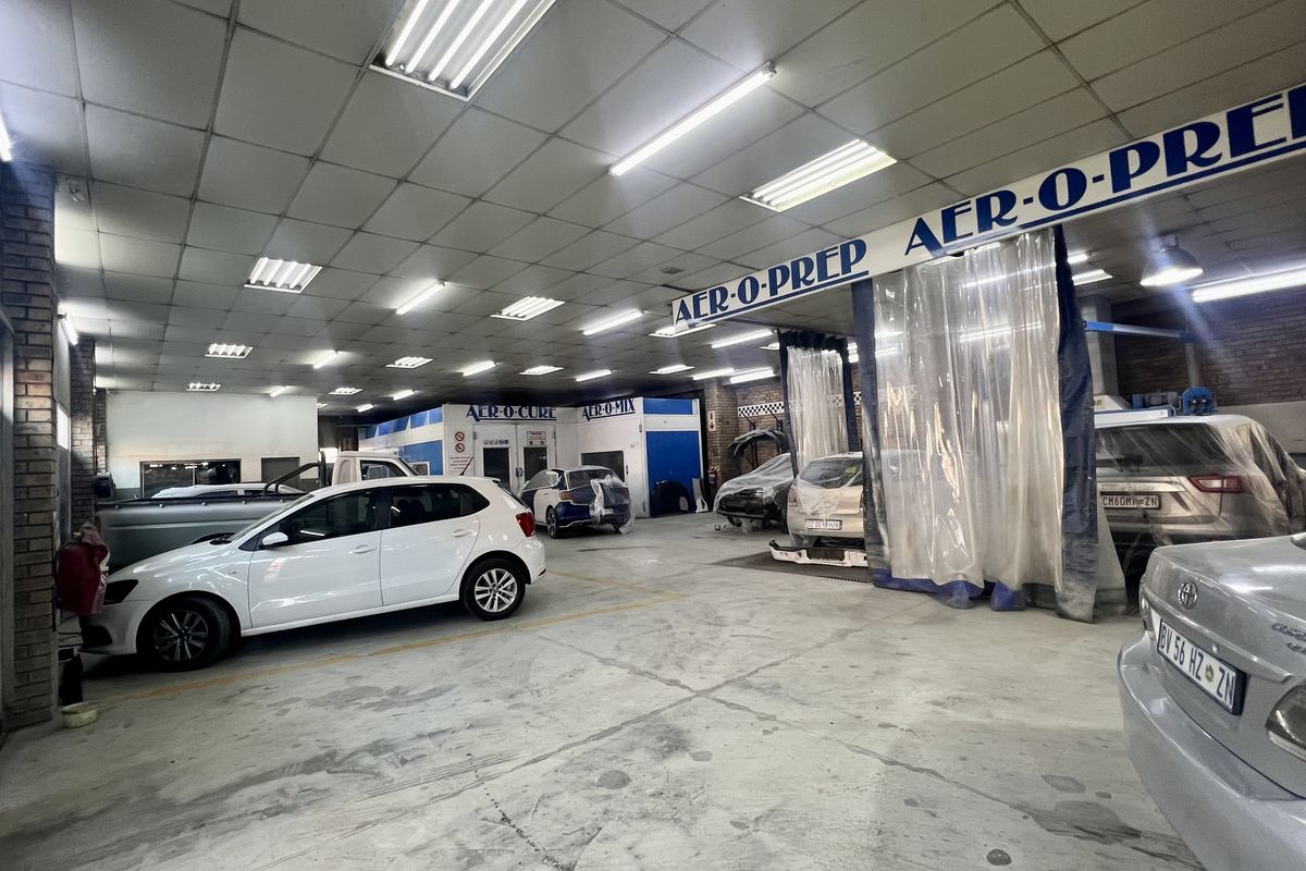 Spacious industrial workshop featuring a dedicated spray booth, suspended lighting, and durable concrete flooring, currently utilized as an automotive repair and preparation facility.
