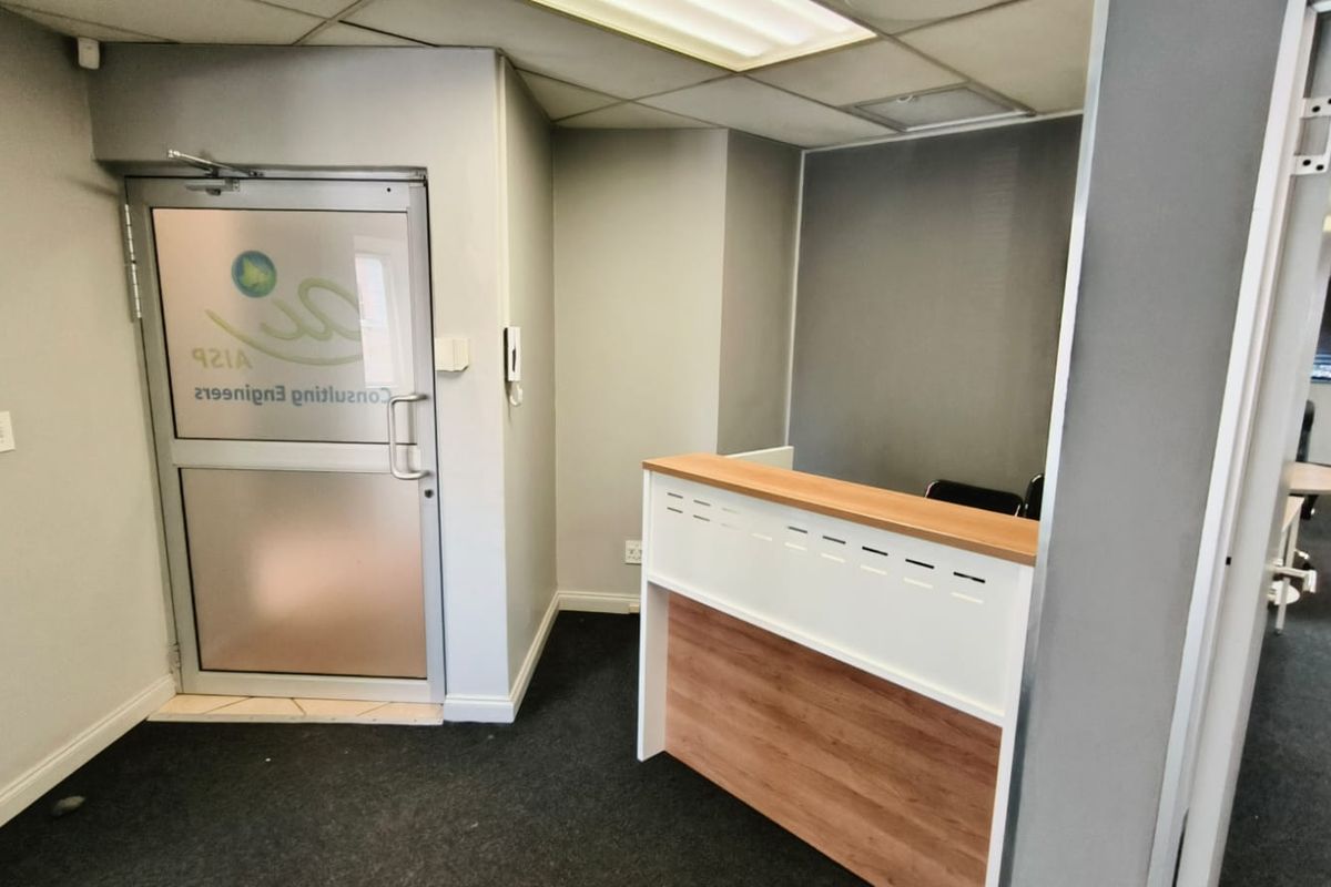 A professional office reception area featuring a built-in desk, suspended ceiling with integrated lighting, and a glass entrance door.