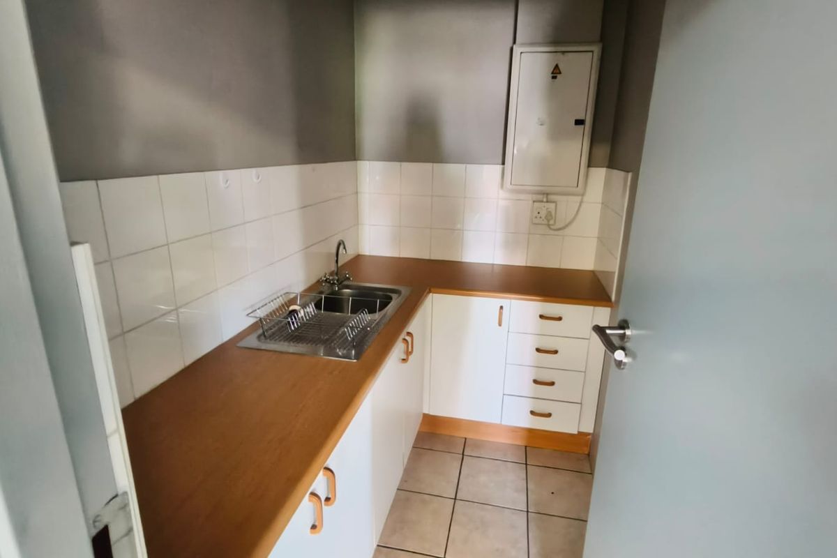A compact kitchenette featuring white cabinetry, wood-look laminate countertops, a stainless steel sink, and tiled backsplash, suitable for office use.