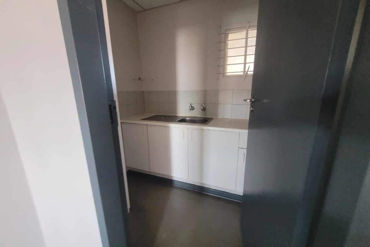 A functional office kitchenette featuring built-in white cabinetry, a stainless steel sink, tiled backsplash, and security bars on the window.