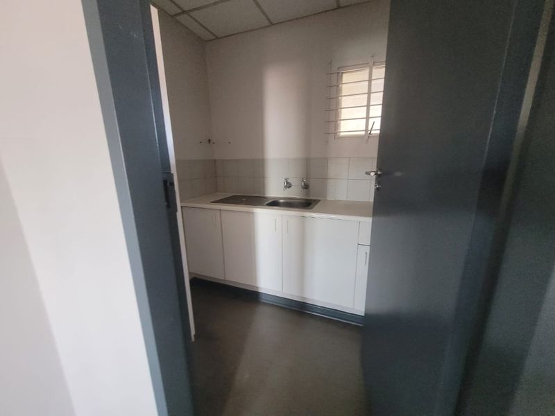 A functional office kitchenette featuring built-in white cabinetry, a stainless steel sink, tiled backsplash, and security bars on the window.