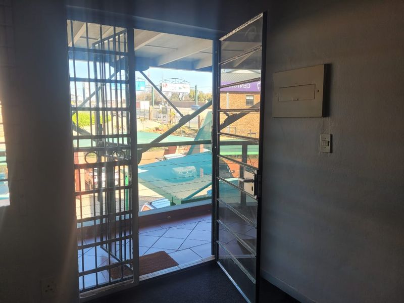 An office entrance area featuring a security gate leading out to a tiled balcony with an electrical distribution board mounted on the wall.