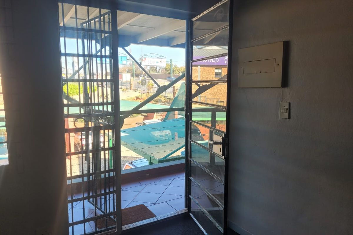 An office entrance area featuring a security gate leading out to a tiled balcony with an electrical distribution board mounted on the wall.