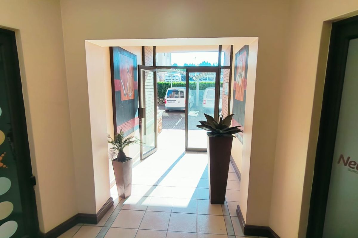 A bright and welcoming office entrance area featuring tiled flooring and glass doors leading to the exterior parking area.