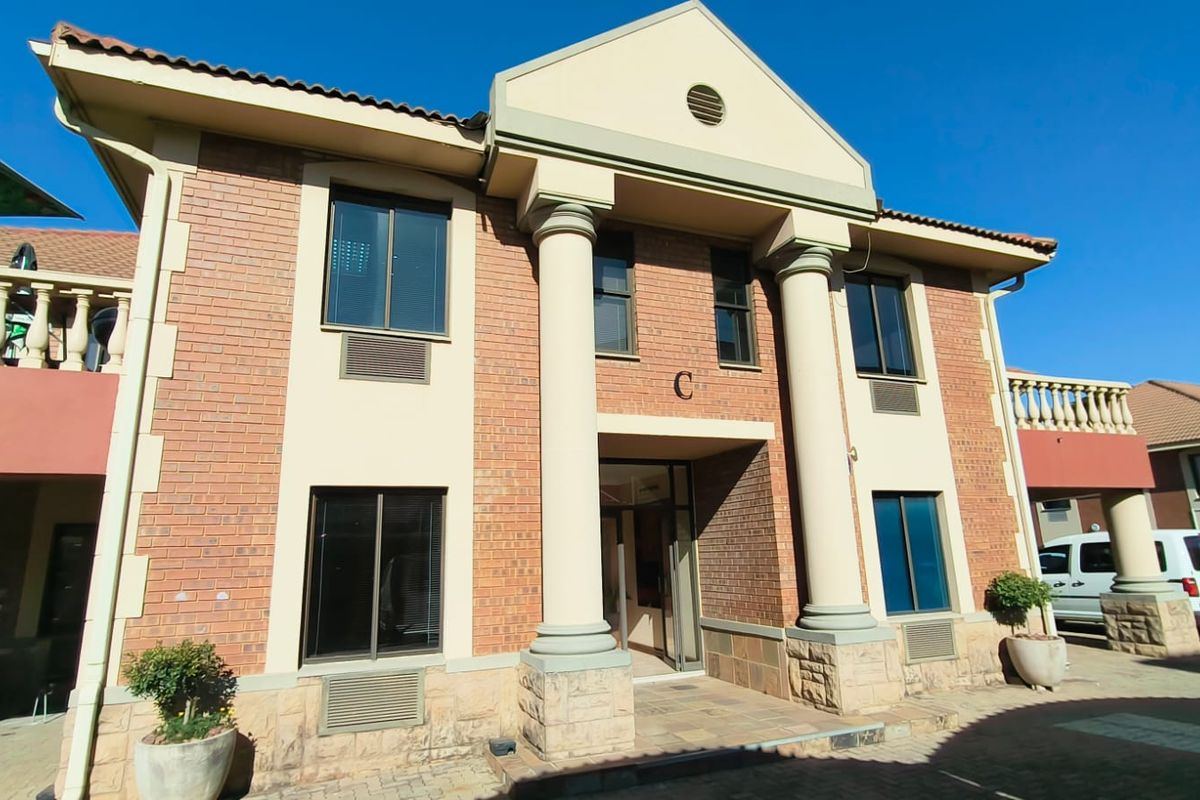 Front elevation of a two-story office building featuring a brick facade, classical columns, and a stone-clad base with a paved entrance area.