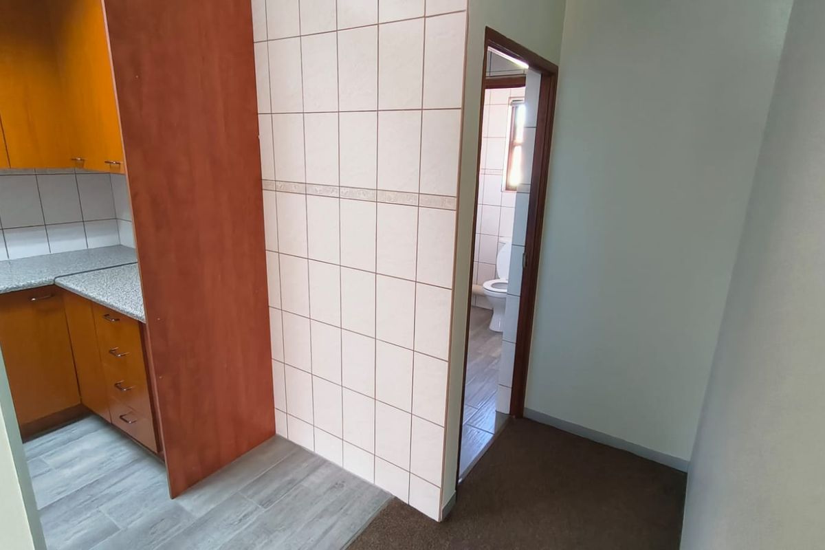 A functional kitchen area featuring built-in wooden cabinetry, tiled splashbacks, and durable flooring, with direct access to an adjacent bathroom facility.