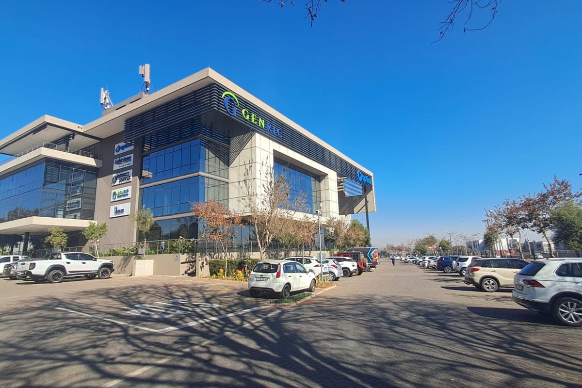 A modern multi-story commercial office building featuring a glass facade, prominent signage, and an extensive paved parking area.