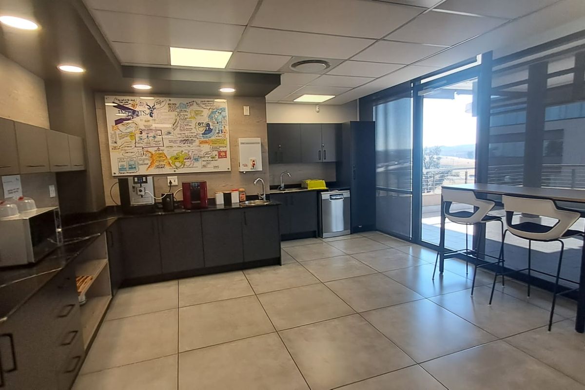 Modern office kitchenette featuring dark cabinetry, tiled flooring, integrated sink, dishwasher, and direct access to an outdoor balcony area.