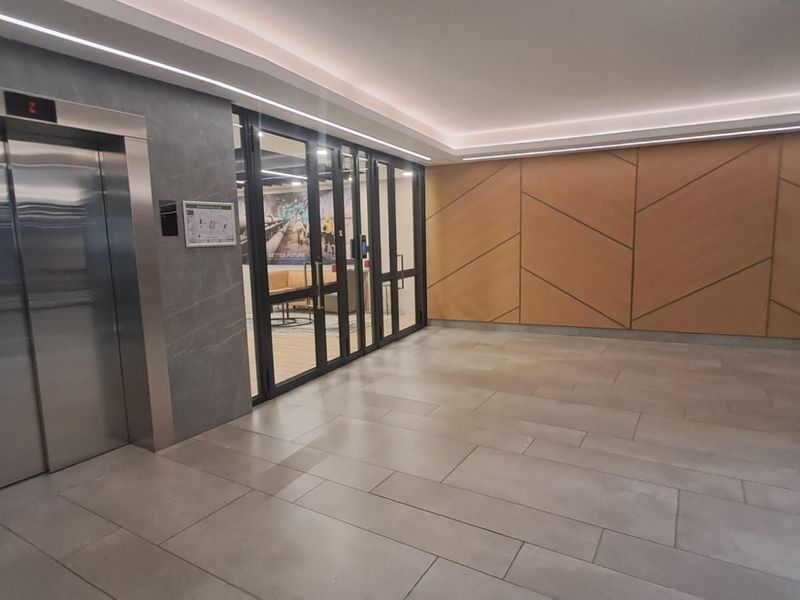 Modern office building lobby featuring a stainless steel elevator, glass partition wall, and decorative timber paneling with recessed lighting.