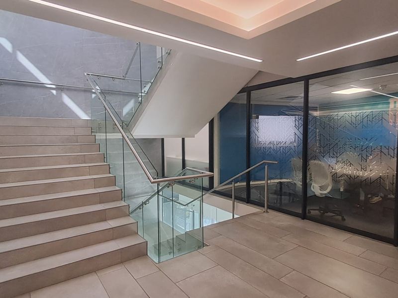 Modern office entrance featuring a tiled staircase with glass balustrades and contemporary recessed lighting, leading to a glass-partitioned workspace.