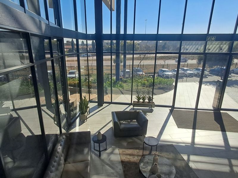 Modern office entrance lobby featuring expansive floor-to-ceiling glass windows, sleek black steel framing, and high-quality tiled flooring with abundant natural light.