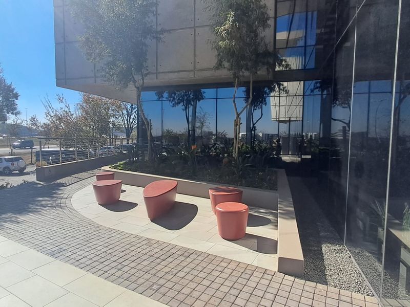 Modern office building exterior featuring a glass curtain wall facade, concrete structural elements, and a paved pedestrian entrance area.