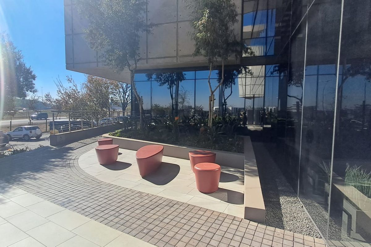 Modern office building exterior featuring a glass curtain wall facade, concrete structural elements, and a paved pedestrian entrance area.