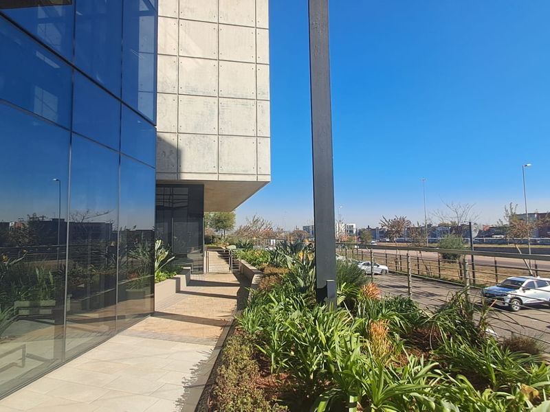 Modern office building exterior featuring a glass curtain wall, concrete facade panels, and a well-maintained landscaped walkway.