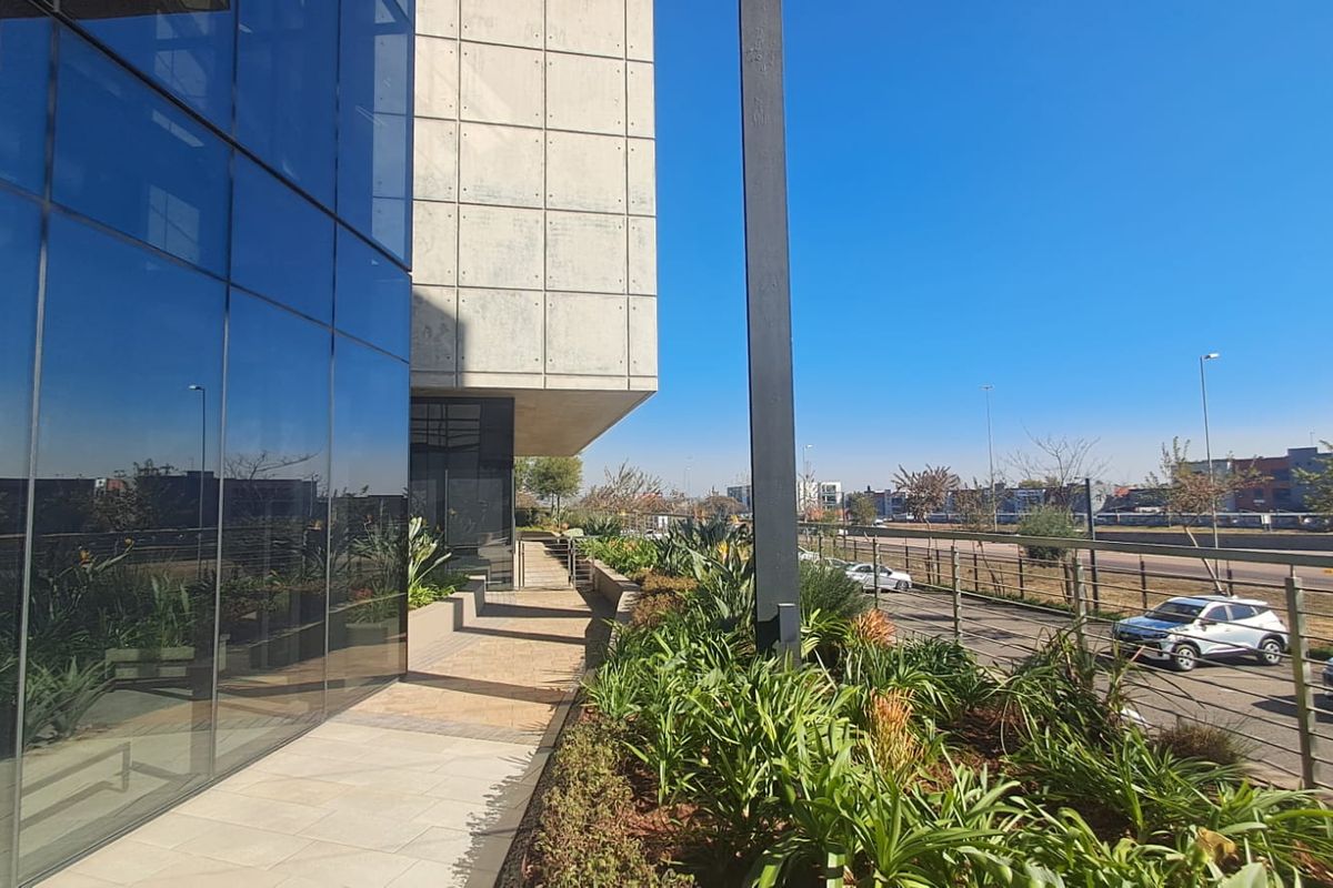 Modern office building exterior featuring a glass curtain wall, concrete facade panels, and a well-maintained landscaped walkway.