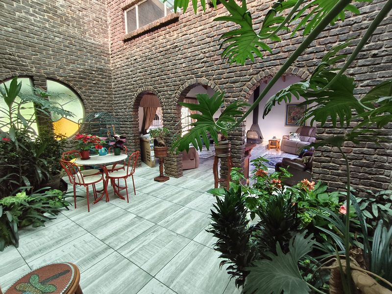 A charming enclosed courtyard patio featuring exposed brick walls, arched architectural details, and large tiled flooring, creating a unique indoor-outdoor living space.