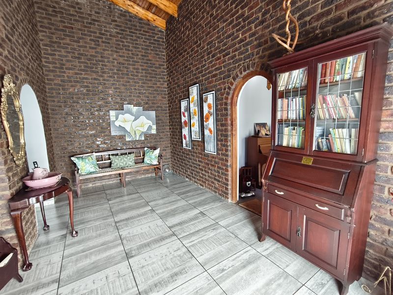 A spacious living area featuring rustic exposed brick walls, a high vaulted timber ceiling, and modern tiled flooring with elegant arched architectural details.
