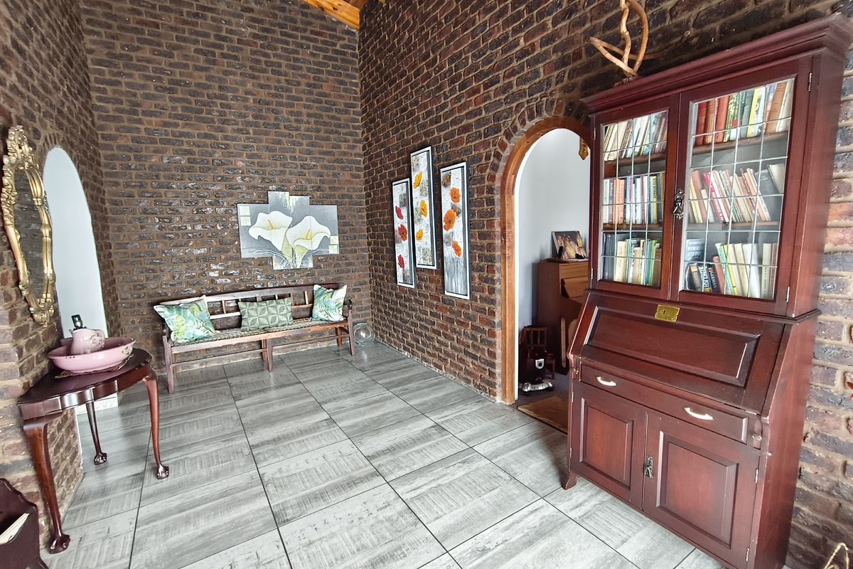 A spacious living area featuring rustic exposed brick walls, a high vaulted timber ceiling, and modern tiled flooring with elegant arched architectural details.