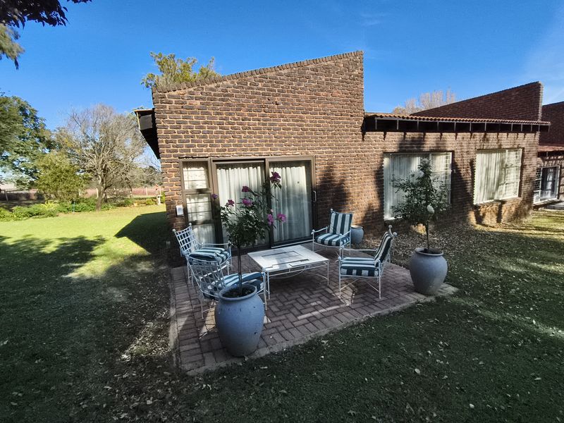 A paved outdoor patio area adjacent to a brick farmhouse building with sliding glass door access to the interior.