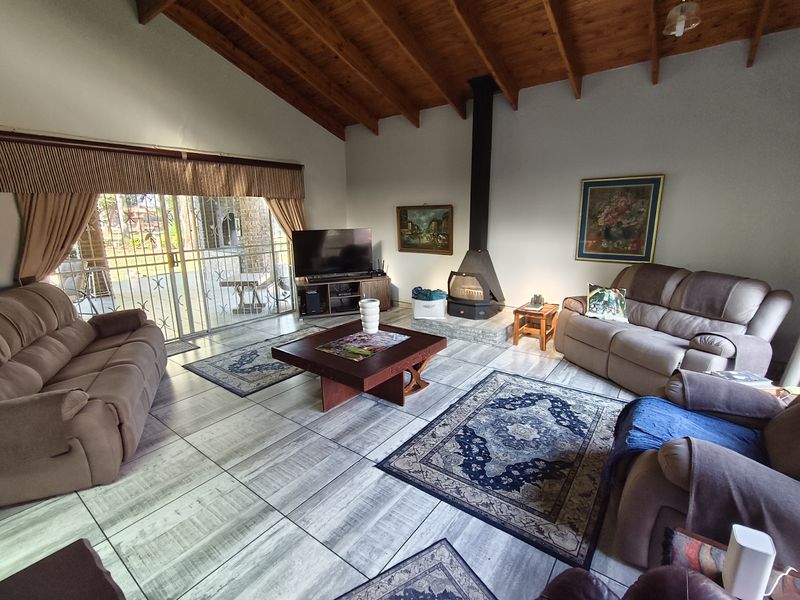 Spacious living room featuring a vaulted timber ceiling, tiled flooring, and a central freestanding fireplace, with direct access to the outdoor patio area.