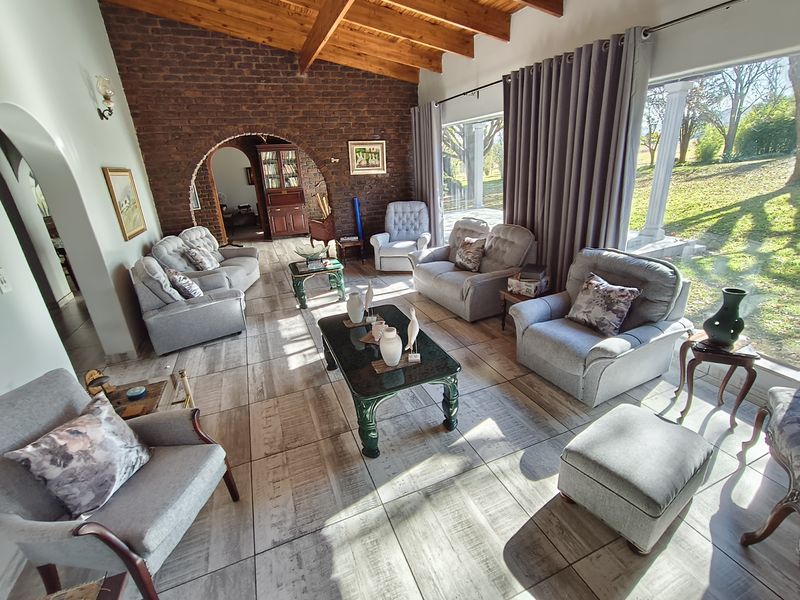 Spacious living room featuring exposed timber beams, a rustic brick feature wall, arched architectural details, and large glass doors opening to the garden.