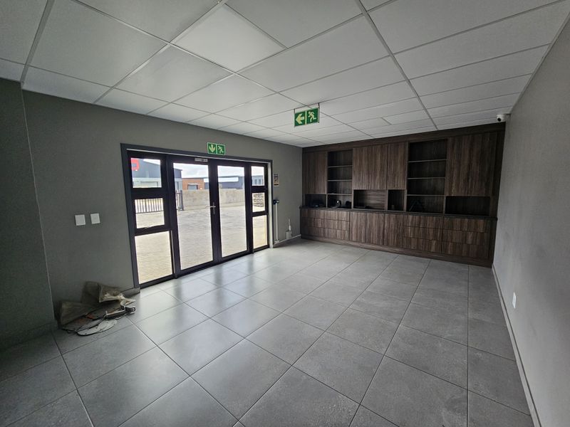 A clean, modern office space featuring large glass entrance doors, neutral tiled flooring, a suspended ceiling, and extensive built-in dark wood cabinetry.