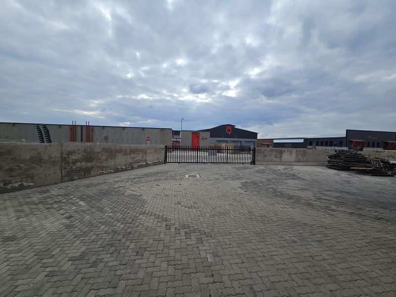 Industrial property exterior featuring a paved yard, concrete perimeter walling, and a secure metal gate entrance to the warehouse facility.