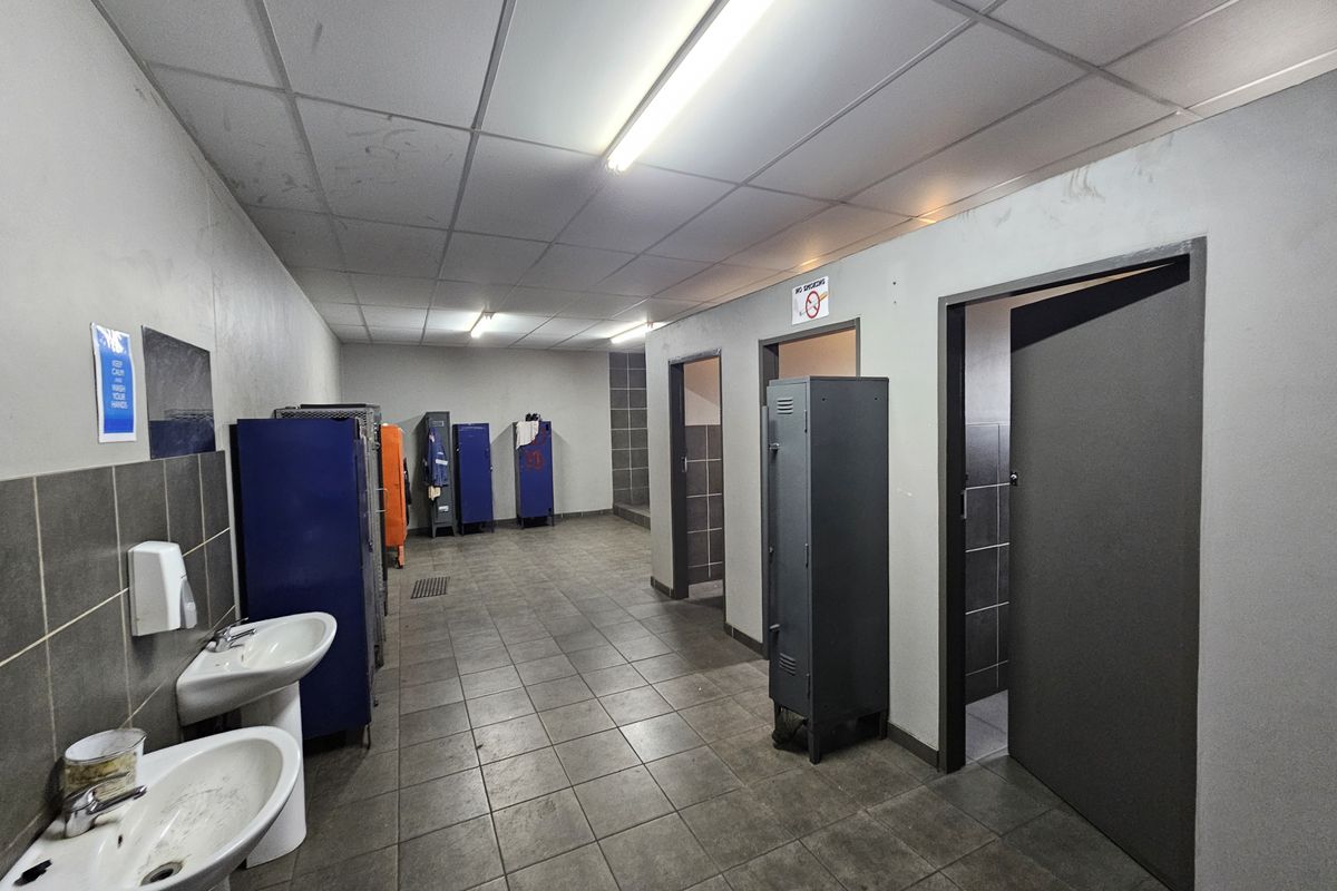 Industrial locker room and bathroom facility featuring pedestal sinks, tiled flooring, and multiple metal storage lockers.