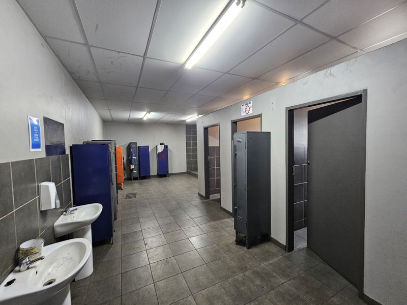 Industrial locker room and bathroom facility featuring pedestal sinks, tiled flooring, and multiple metal storage lockers.