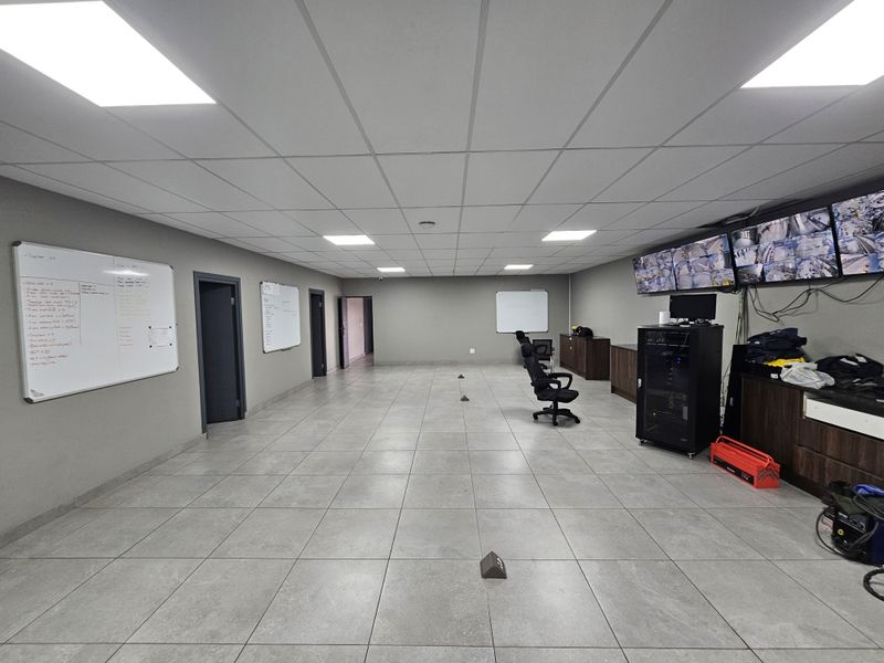 A spacious industrial office area featuring tiled flooring, suspended ceilings with recessed lighting, and a dedicated CCTV monitoring station with built-in cabinetry.
