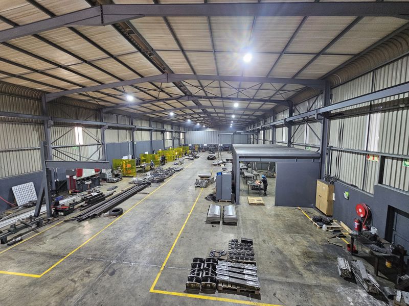 Spacious industrial warehouse featuring a high-clearance steel portal frame, concrete flooring, and functional overhead lighting, suitable for manufacturing or storage operations.