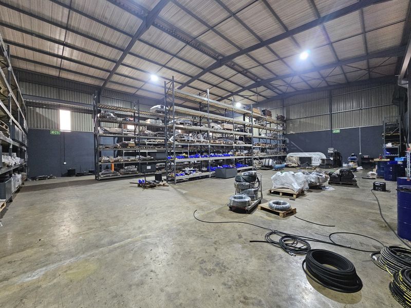 Spacious industrial warehouse featuring high ceilings, exposed steel roof trusses, durable concrete flooring, and extensive built-in steel racking systems for storage.