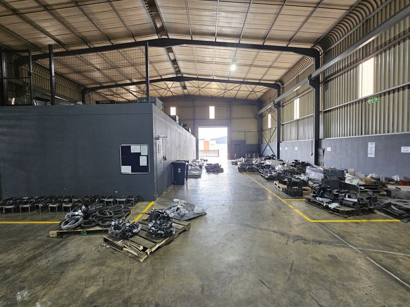 Spacious industrial warehouse unit featuring high ceilings, concrete flooring, a mezzanine level, and large roller shutter access, suitable for storage or manufacturing operations.