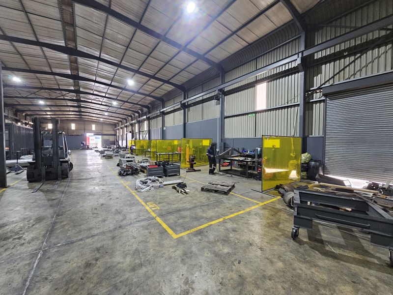 Spacious industrial warehouse featuring a steel portal frame, high-bay lighting, concrete flooring, and integrated welding bays with protective screens.