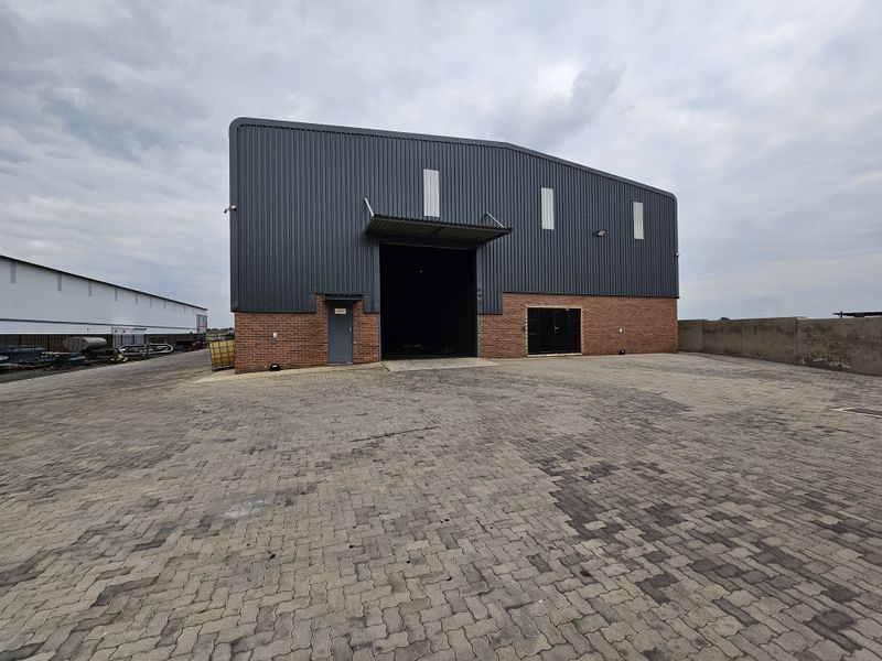 Industrial warehouse facility featuring a large roller shutter door, brick and metal cladding exterior, and a spacious paved yard area.