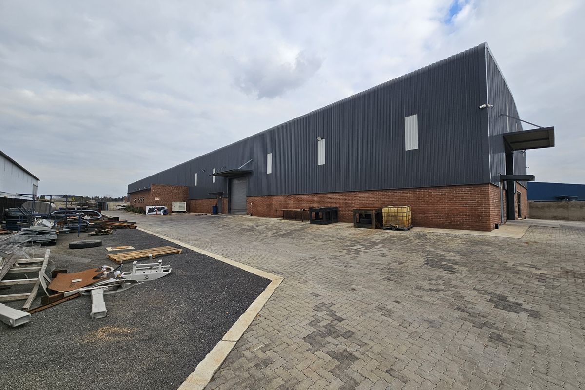 Industrial warehouse exterior featuring a combination of brick and corrugated metal cladding with a paved yard area and roller shutter access.