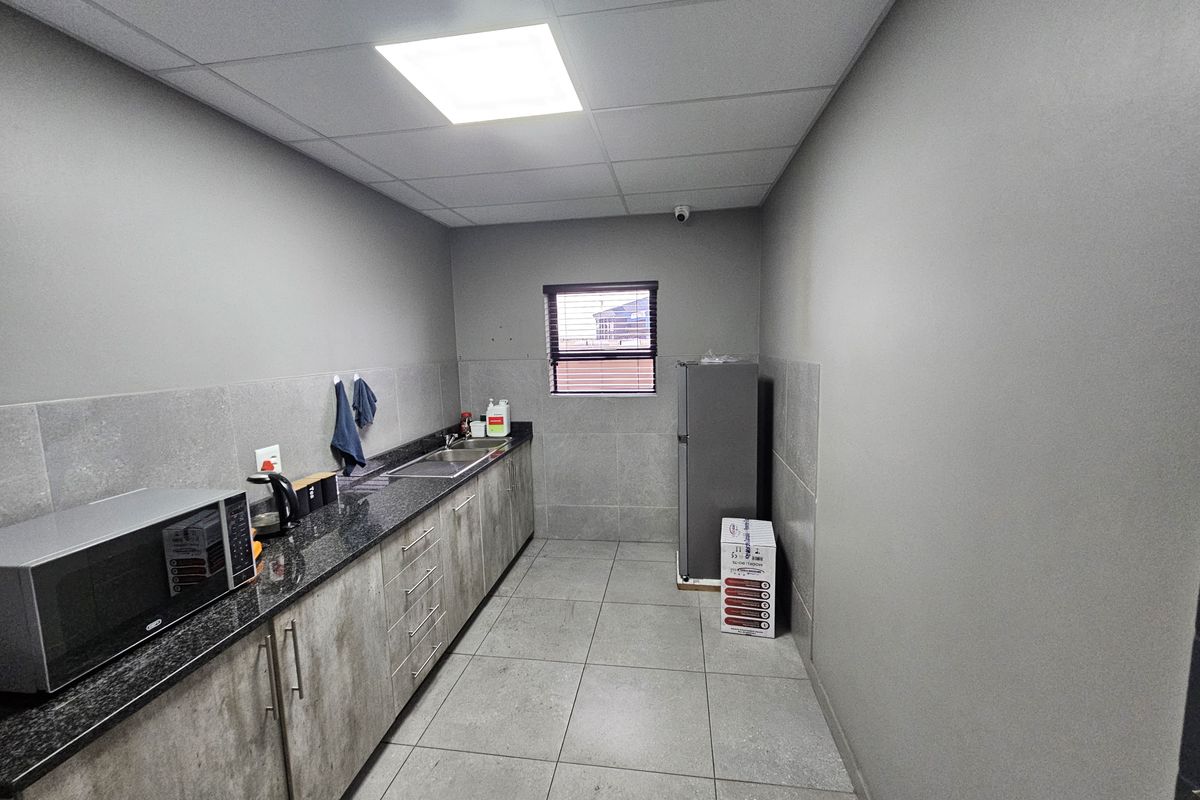 A clean, modern industrial kitchen featuring granite countertops, ample built-in cabinetry, tiled flooring, and a functional sink area with recessed lighting.
