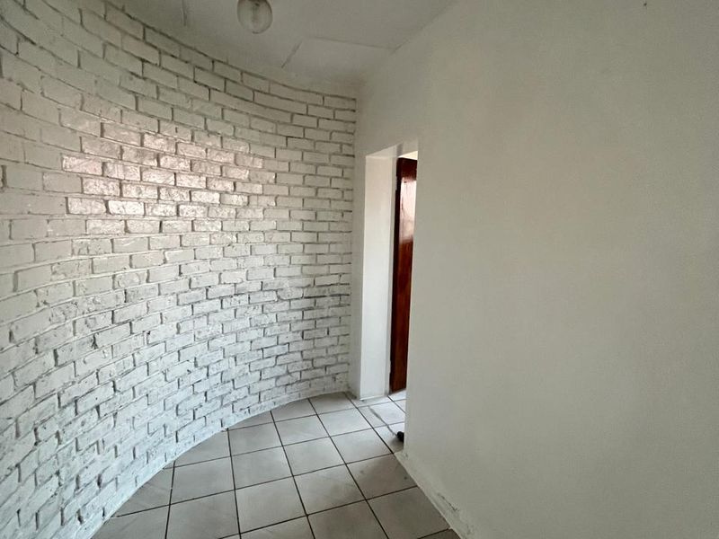 A vacant hallway featuring a distinctive curved white brick wall and ceramic tiled flooring, leading to an interior doorway.