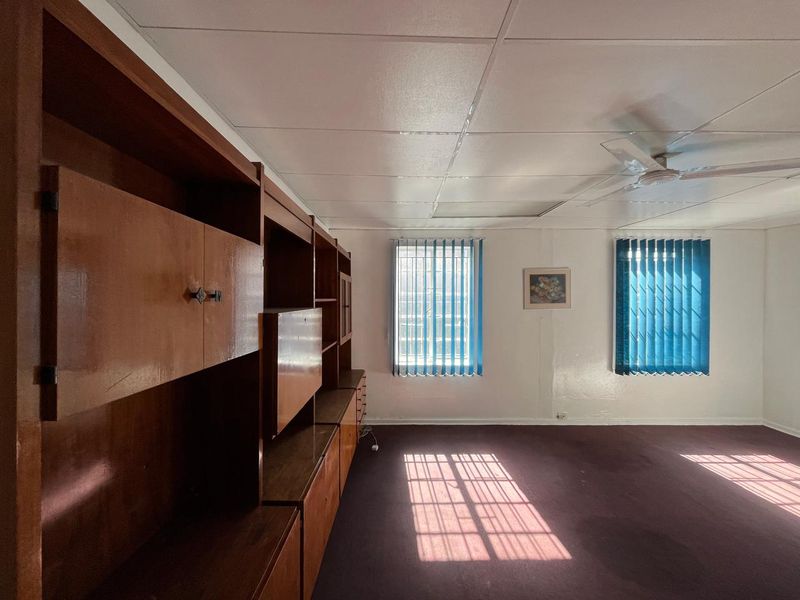 Spacious office area featuring built-in wooden cabinetry, vertical window blinds, a ceiling fan, and suspended ceiling tiles.