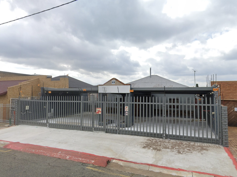 Front exterior view of a commercial property featuring a secure metal gate, electric fencing, and a concrete driveway.