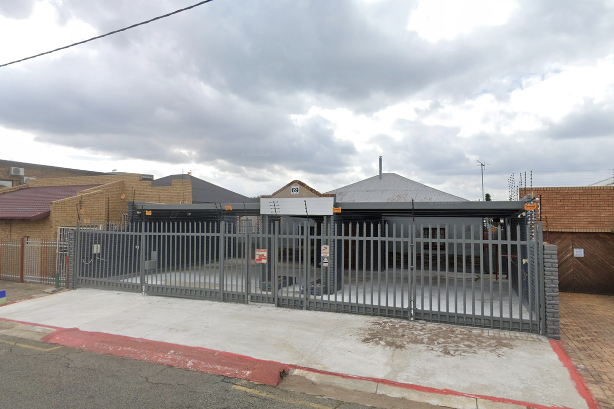 Front exterior view of a commercial property featuring a secure metal gate, electric fencing, and a concrete driveway.