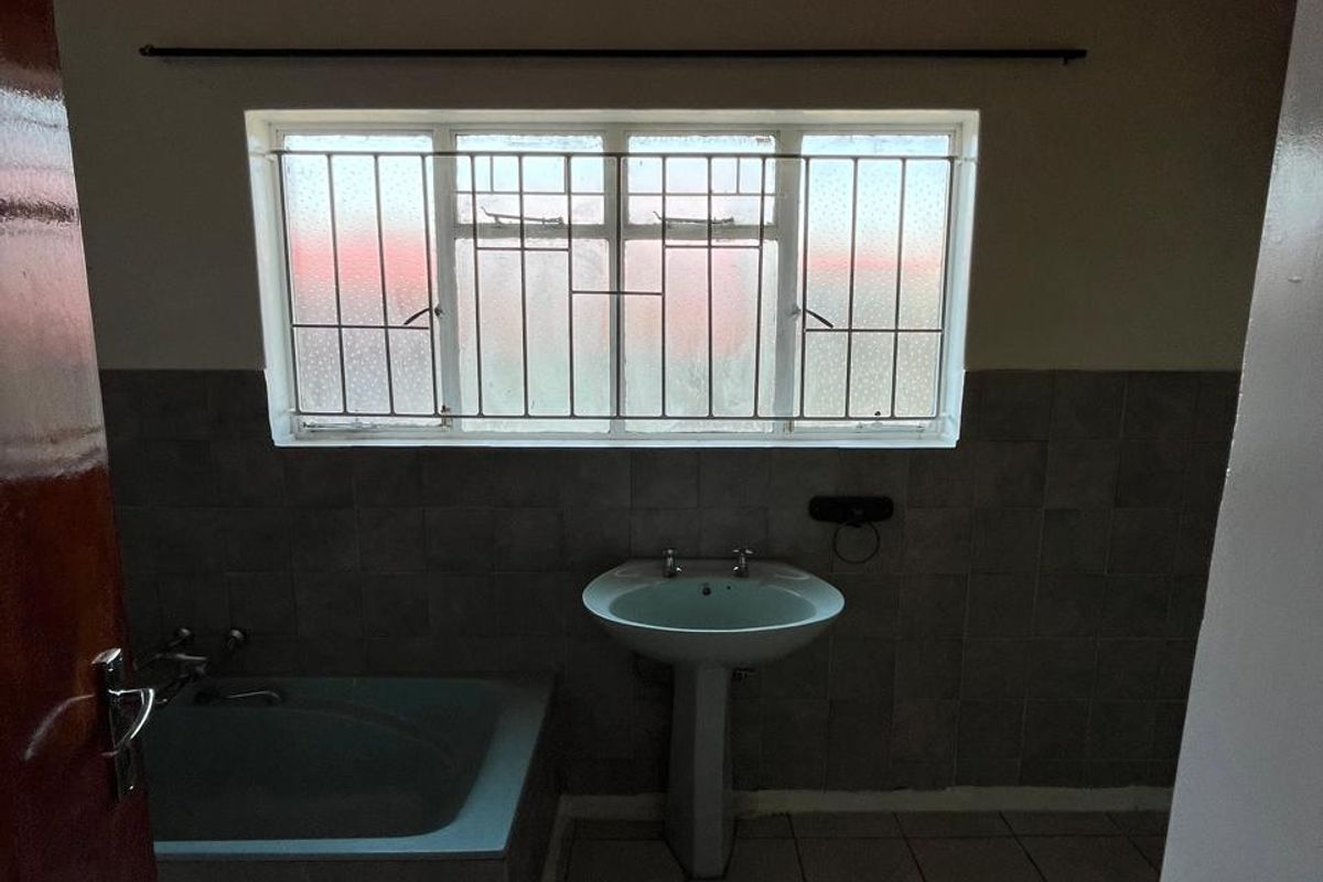 A functional bathroom featuring a pedestal basin, built-in bathtub, tiled flooring, and a timber ceiling, offering a blank canvas for renovation.