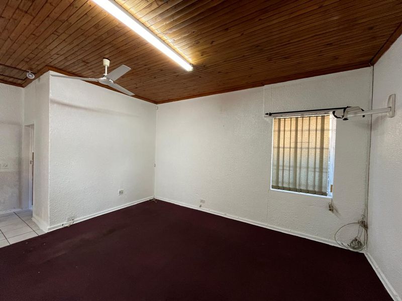 An empty office space featuring a timber ceiling, ceiling fan, vertical blinds, and carpet flooring, suitable for a professional workspace.