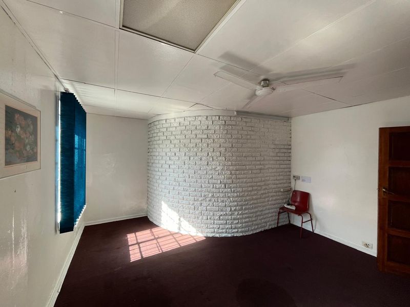An empty office space featuring a unique curved white brick wall, suspended ceiling tiles, and a ceiling fan.