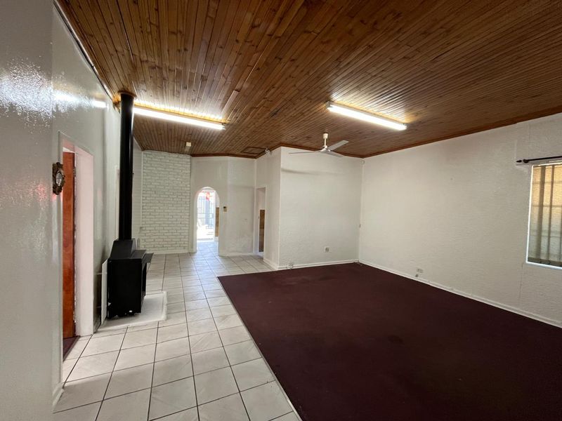 Spacious living area featuring a wood-paneled ceiling, a freestanding fireplace, and a mix of tiled and carpeted flooring.