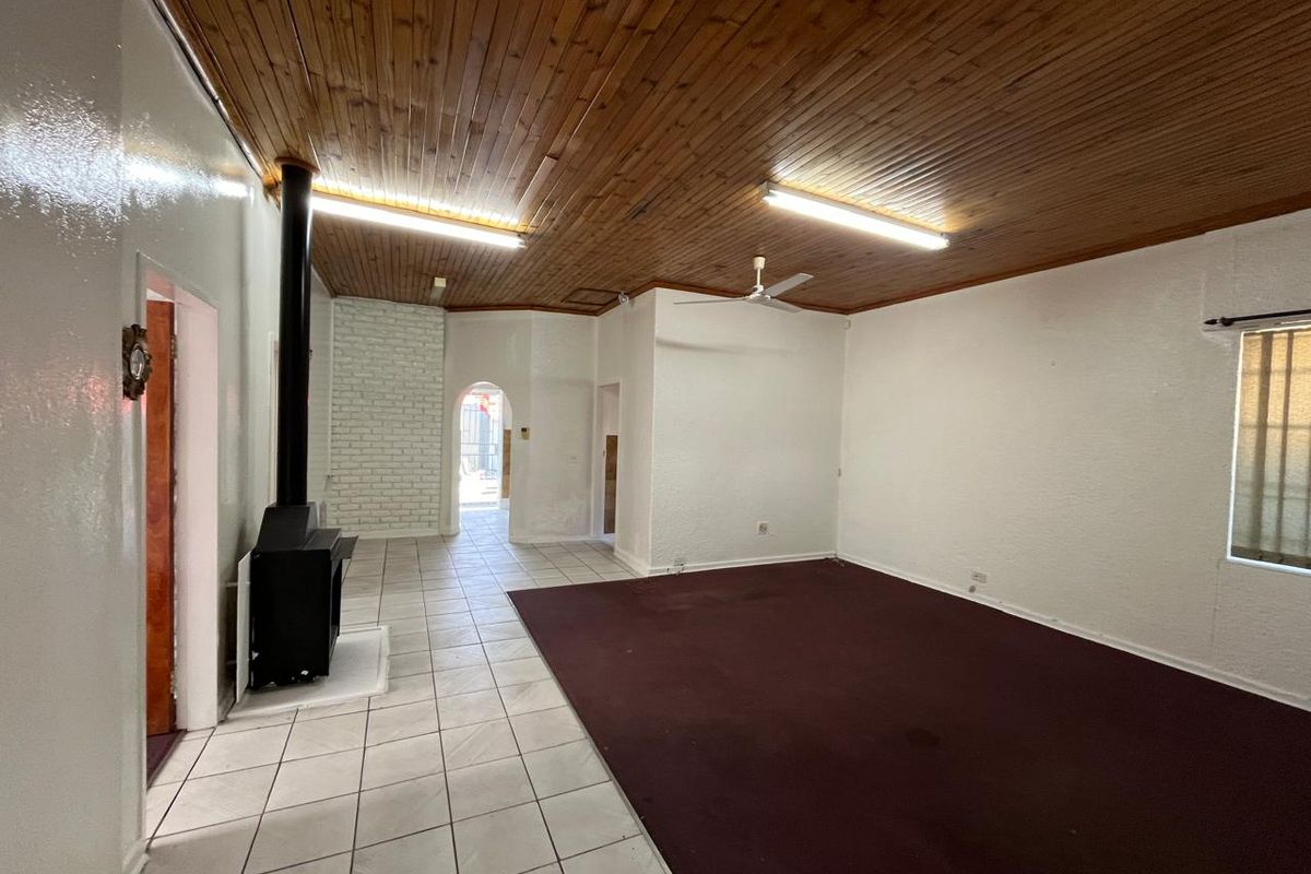 Spacious living area featuring a wood-paneled ceiling, a freestanding fireplace, and a mix of tiled and carpeted flooring.