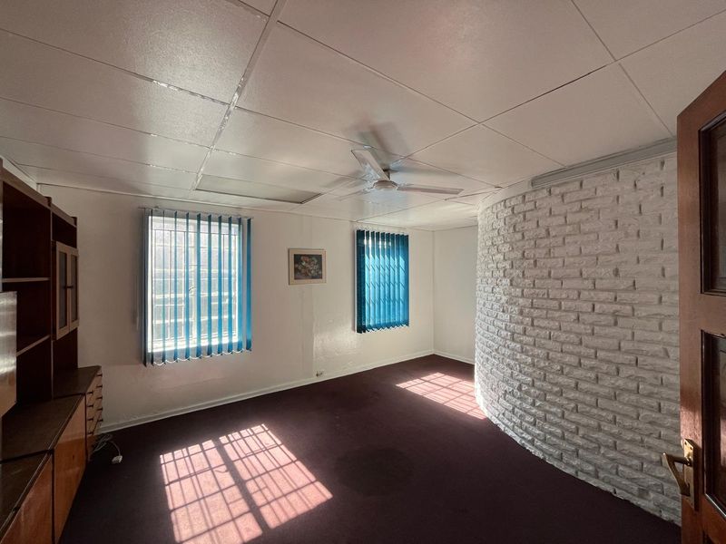 Office space featuring a distinctive curved white brick wall, suspended ceiling with fan, and built-in storage cabinetry.