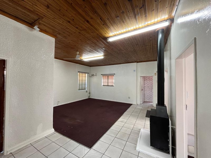 Spacious living area featuring a wood-paneled ceiling, tiled flooring, and a built-in fireplace, offering a versatile layout for commercial or office use.