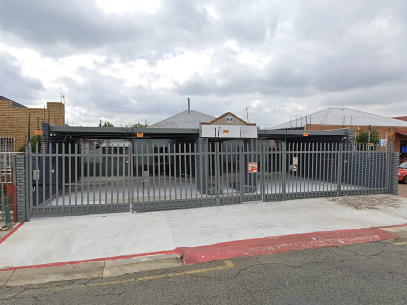 Front exterior view of a commercial property featuring a secure steel gate, electric fencing, and a covered carport area.