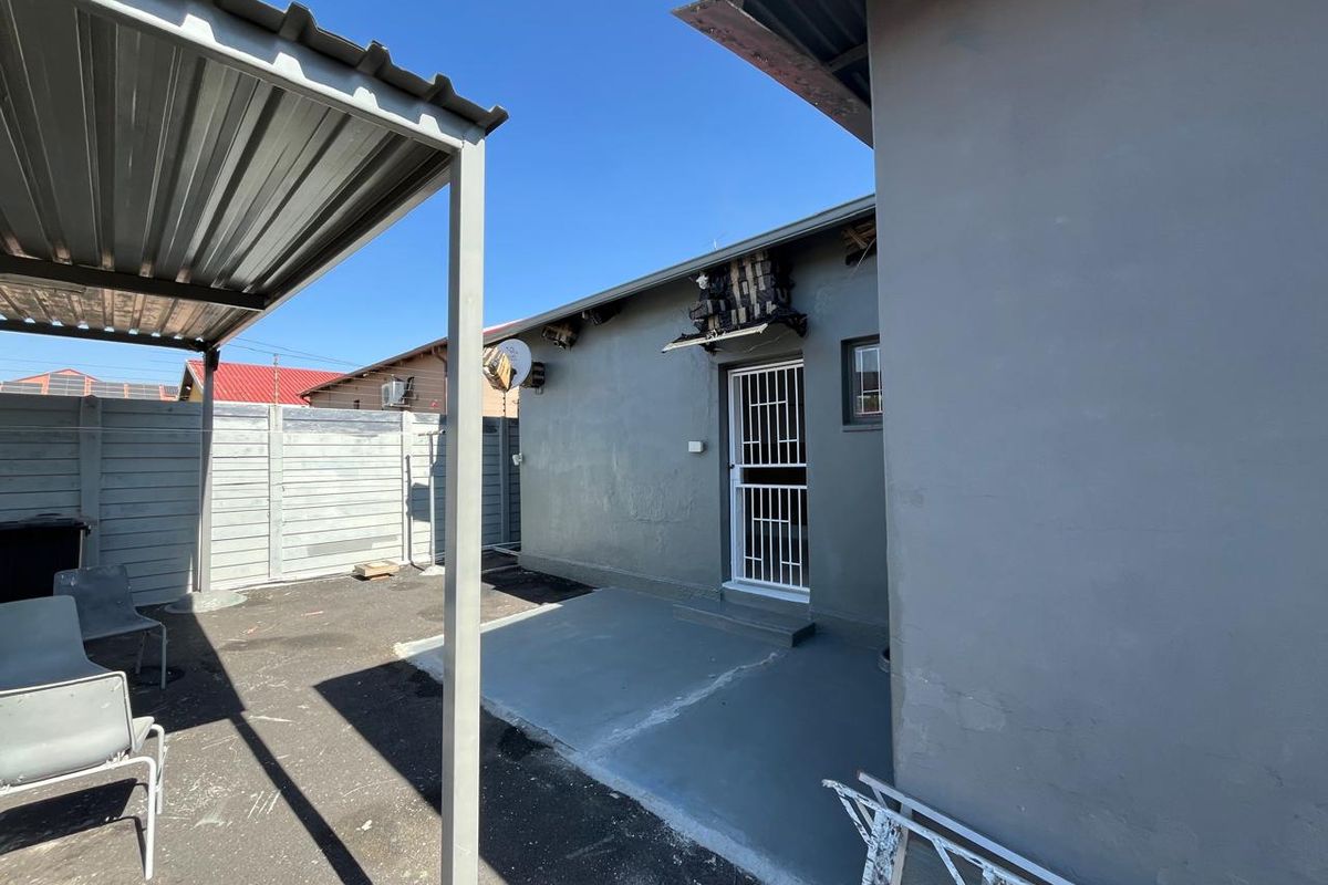 Rear exterior view of the property featuring a concrete patio, corrugated metal roof structure, and perimeter precast concrete walling.